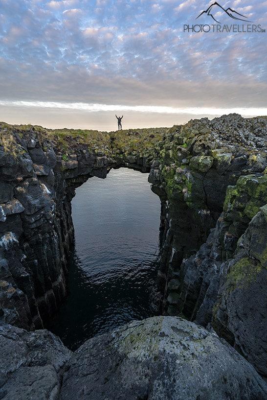 Blogueuse de voyage Biggi Bauer sur un immense arc rocheux dans la mer sur la côte d'Arnarstapi en Islande