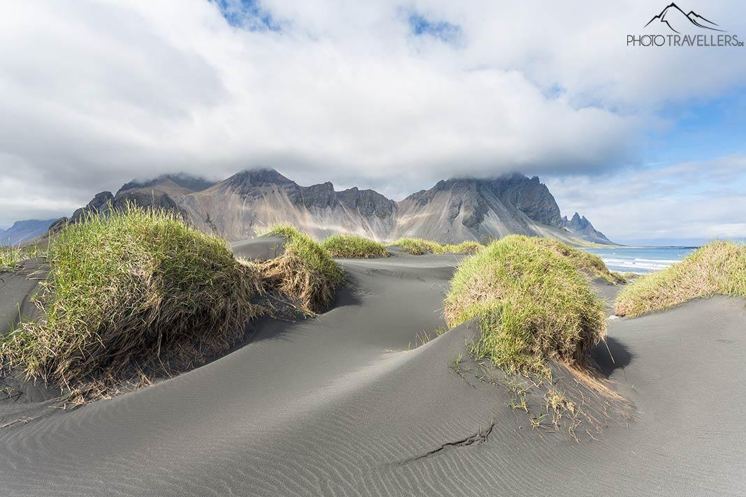 Plage de sable noir et collines herbeuses à Stokksnes, avec des montagnes en arrière-plan