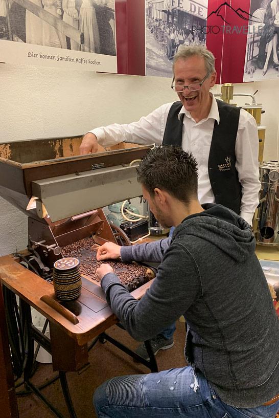 O jornalista de viagem Florian Westermann sentado na seleção de café da torrefação Krimse, o chefe da torrefação, Jens Kirmse, observa