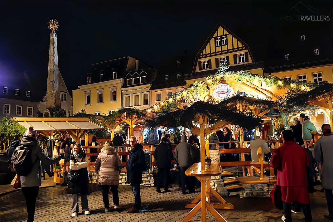 De nombreuses personnes se tiennent devant les stands illuminés devant les maisons à colombages sur la place du marché de Kulmbach.