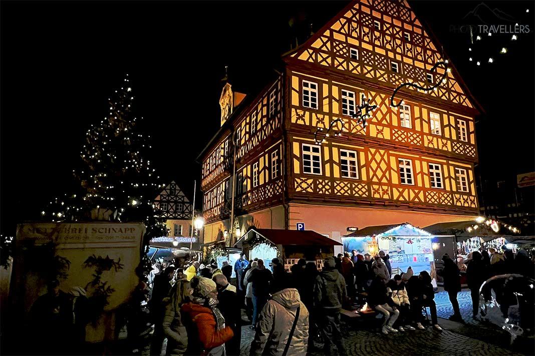 Devant la maison à colombages éclairée à Bad Staffelstein, de nombreuses personnes se tiennent devant les stands de Noël.
