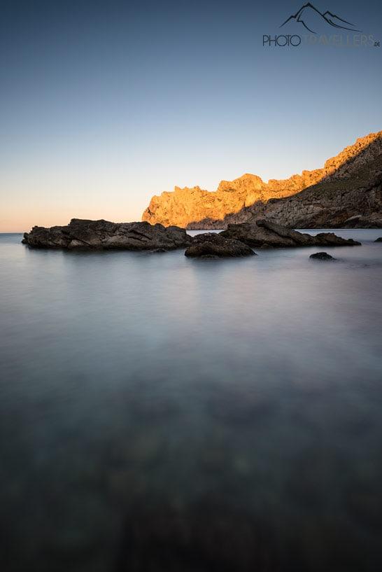 A praia de Cala Sant Vicenç com vista para altas falésias que são iluminadas pelo sol à noite