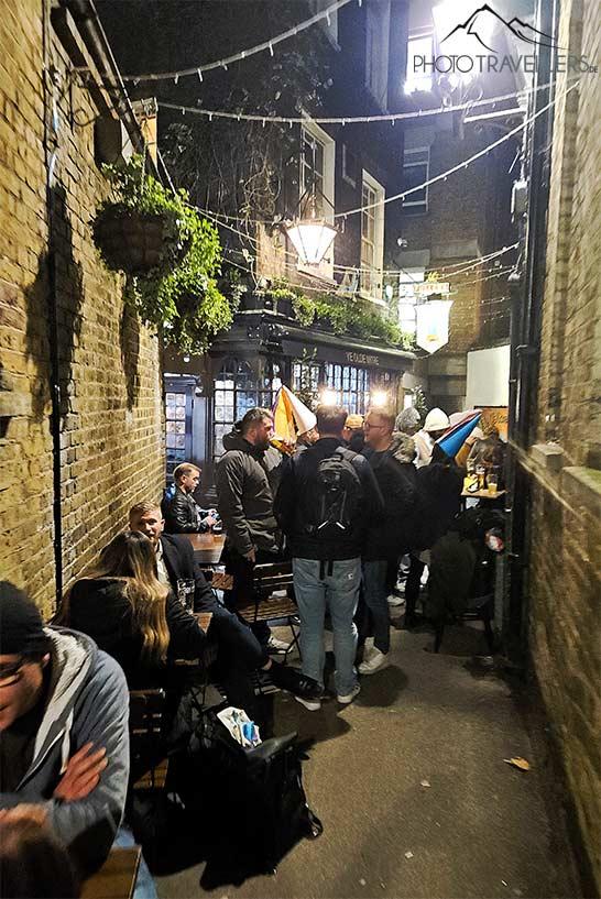 Dans une ruelle étroite se tiennent de nombreux clients du pub Ye Olde Mitre, buvant de la bière