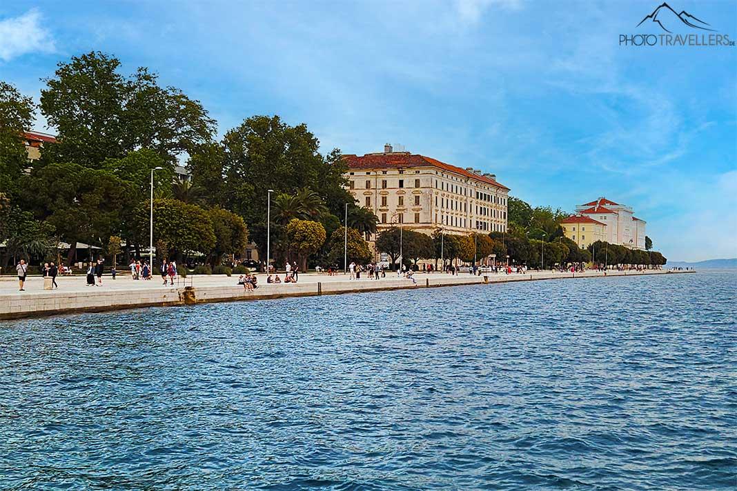 Des piétons se promènent le long de la promenade Riva avec des arbres et des maisons en arrière-plan