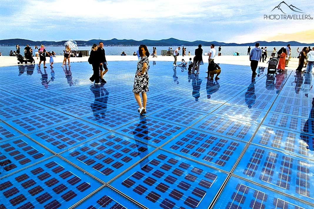 Des gens se tiennent sur le sol en verre bleu de la promenade de Zadar