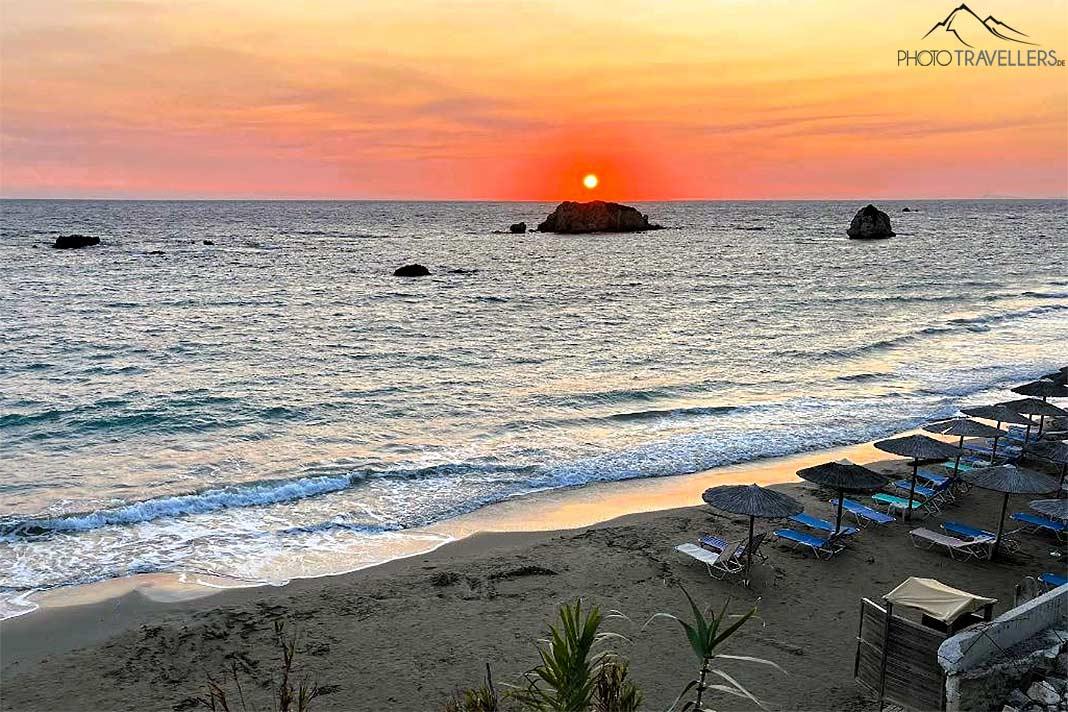 Playa de arena con tumbonas con rocosa puesta de sol detrás