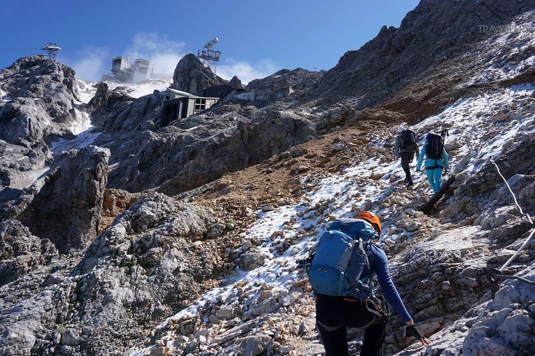 La journaliste de voyage Biggi Bauer et deux randonneurs devant l'ancienne et la nouvelle station de montagne de la Tiroler Zugspitzbahn