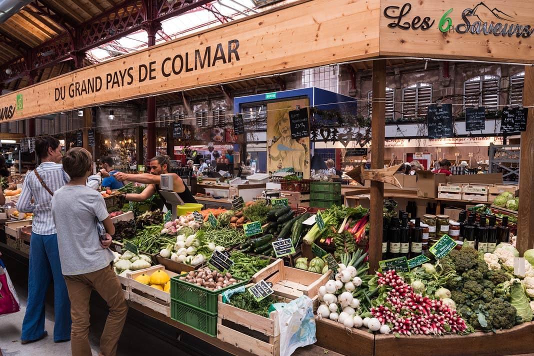Des clients devant un stand de légumes dans la halle couverte à Colmar