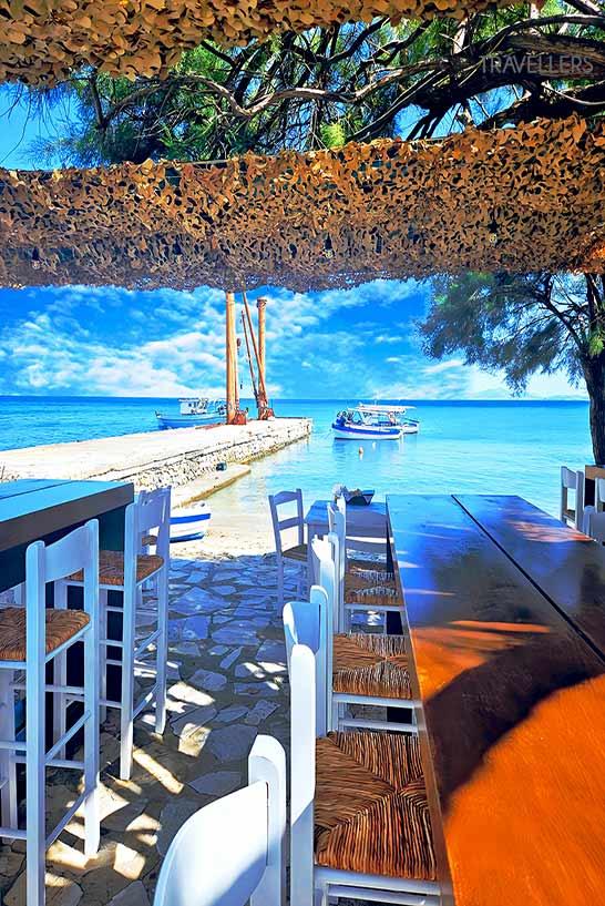 Mesas ficam sob árvores à beira da praia da vila de pescadores Moutsouna