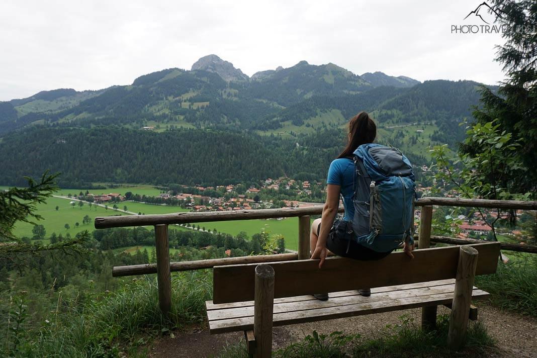 La blogueuse voyage Biggi Bauer est assise sur un banc et regarde Bayrischzell en bas. En arrière-plan, le Wendelstein s'élève vers le ciel.