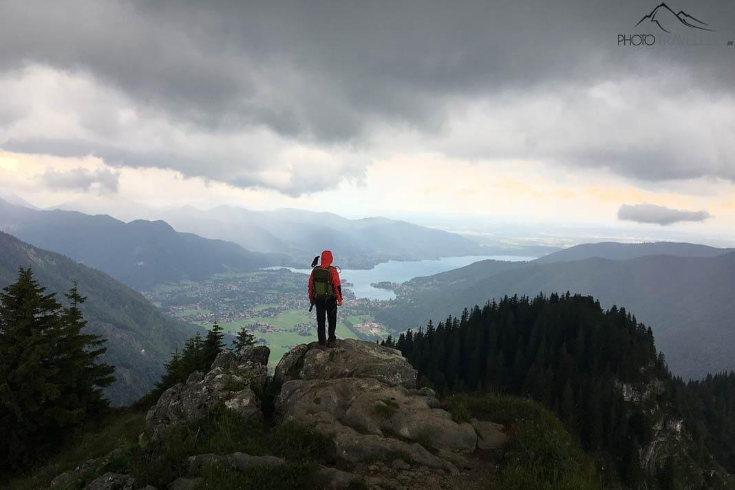 Un participant de la formation de guide de randonnée sur un rocher avec vue sur le Tegernsee