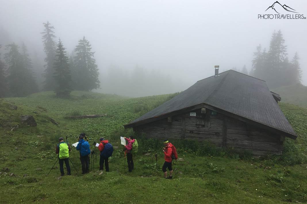 Cinq participants de la formation de guide de randonnée avec des cartes devant une cabane de montagne dans le brouillard