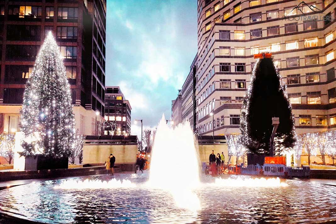 Fonte iluminada e árvores de Natal em frente aos prédios altos de Canary Wharf