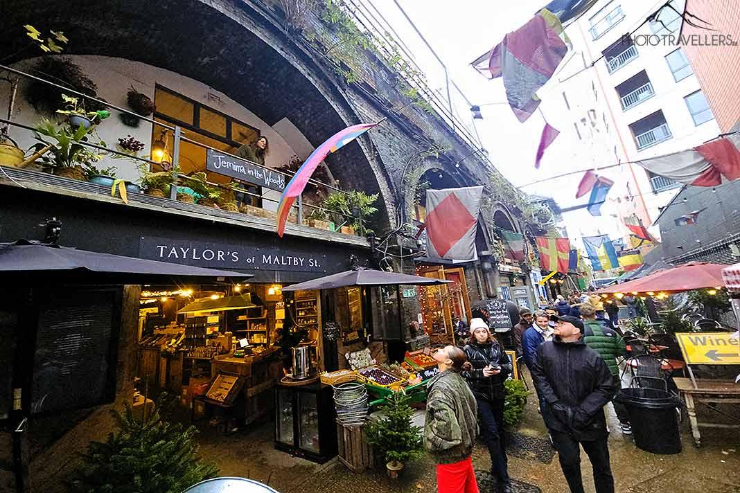 Des visiteurs se rassemblent sous les arches du viaduc ferroviaire sur Maltby Street pour observer l'animation du marché