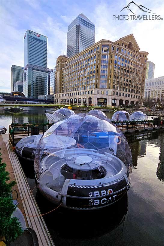 Plusieurs igloos flottants avec un toit en verre bordent le canal devant les immeubles de Canary Wharf