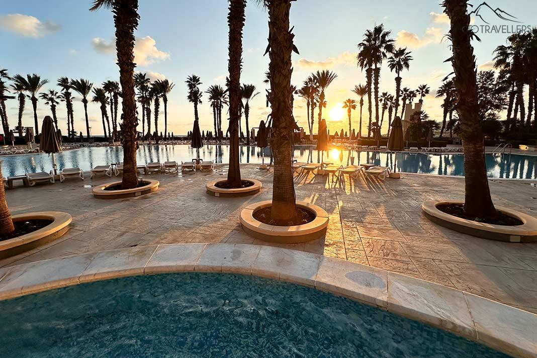 O sol nasce sobre a piscina com palmeiras do Hilton Hotel em Malta