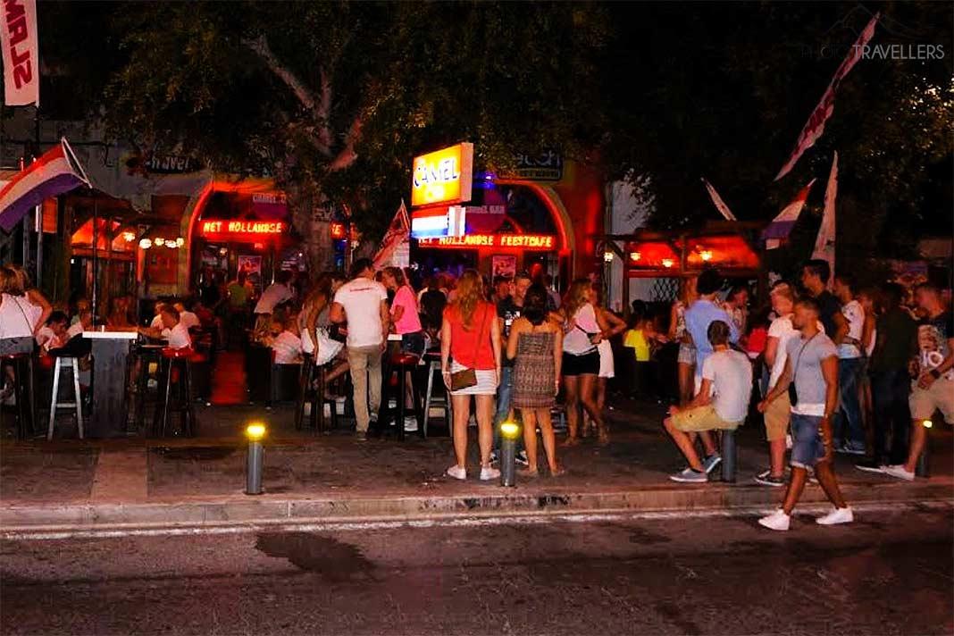 De nombreux jeunes se tiennent devant une discothèque illuminée de couleurs vives dans la ville de Kos.