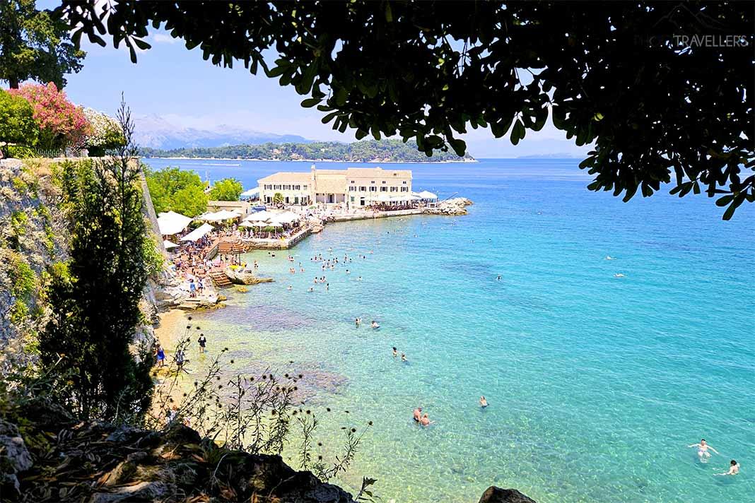 Muitas pessoas se aglomeram nas praias entre rochas e árvores em Corfu