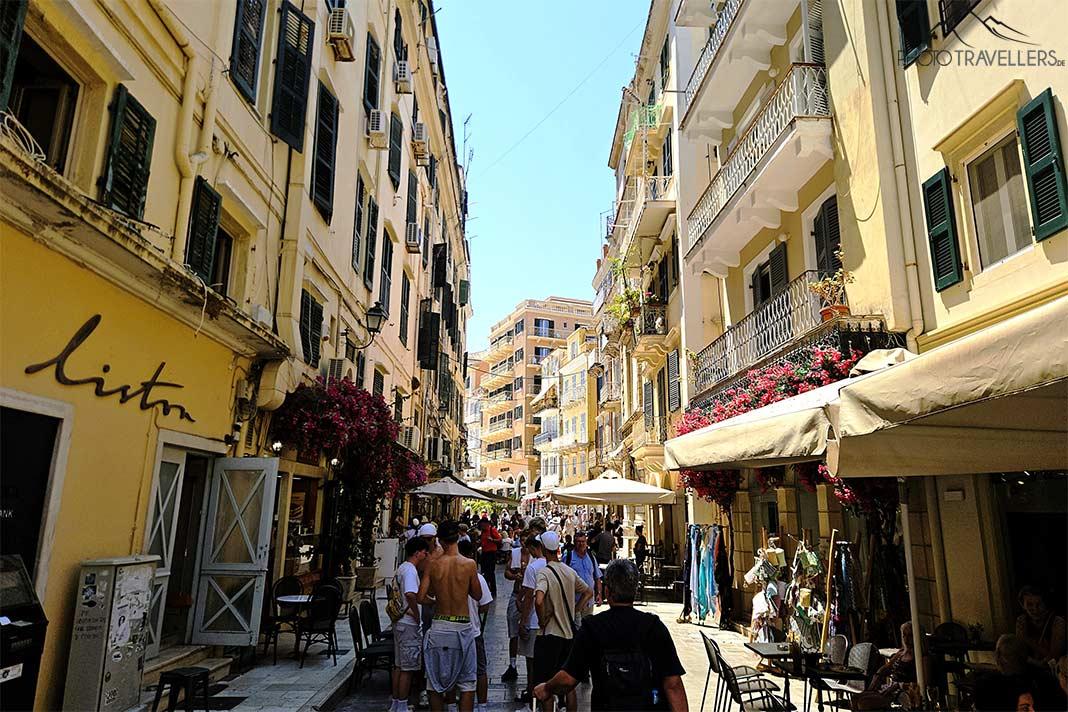 Muitas pessoas passeiam pelas ruas da cidade velha de Kerkyra, cercadas por fachadas amarelas