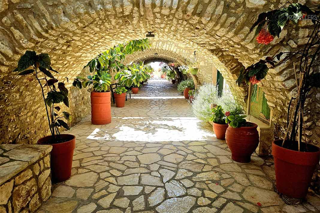 Un largo pasillo de arcos de piedra y macetas conduce al monasterio de Paleokastritsa