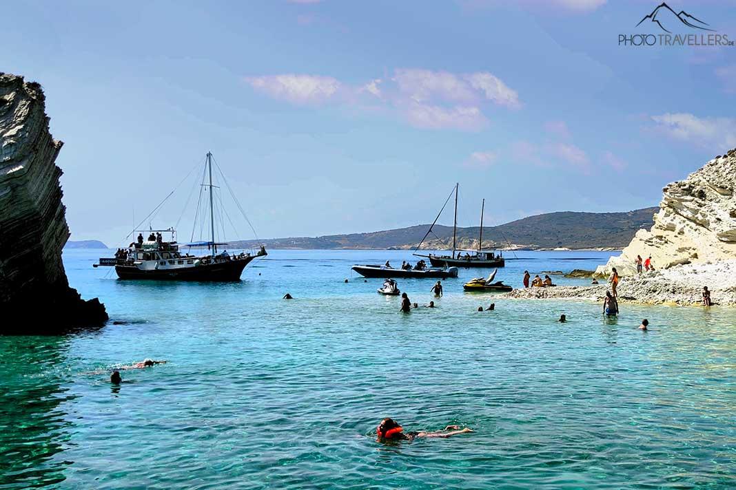 Botes y personas nadan en el mar frente a los acantilados de caliza