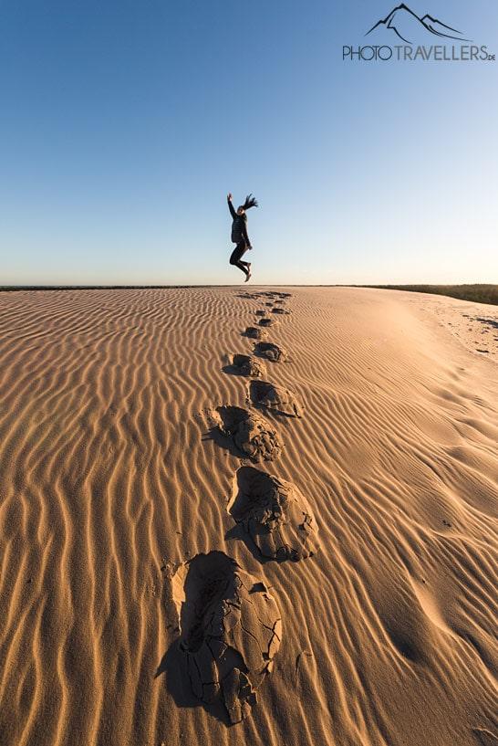La blogueuse voyage Biggi Bauer saute de la dune mobile Råbjerg Mile. Devant elle, on voit de profondes empreintes de pas dans le sable