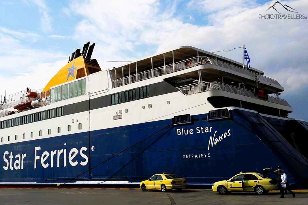 Dos taxis esperan frente a un gran ferry azul y blanco en el puerto de Paros