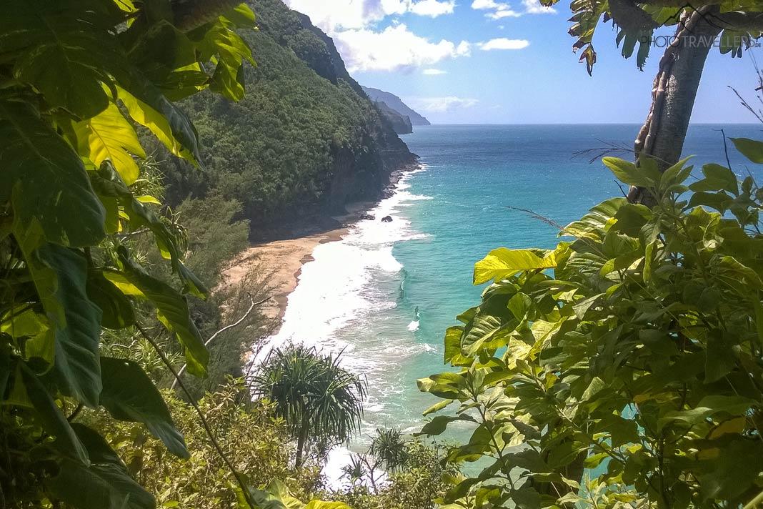 A vista do Kalalau Trail através das folhas para o Hanakapiai Beach com o mar turquesa