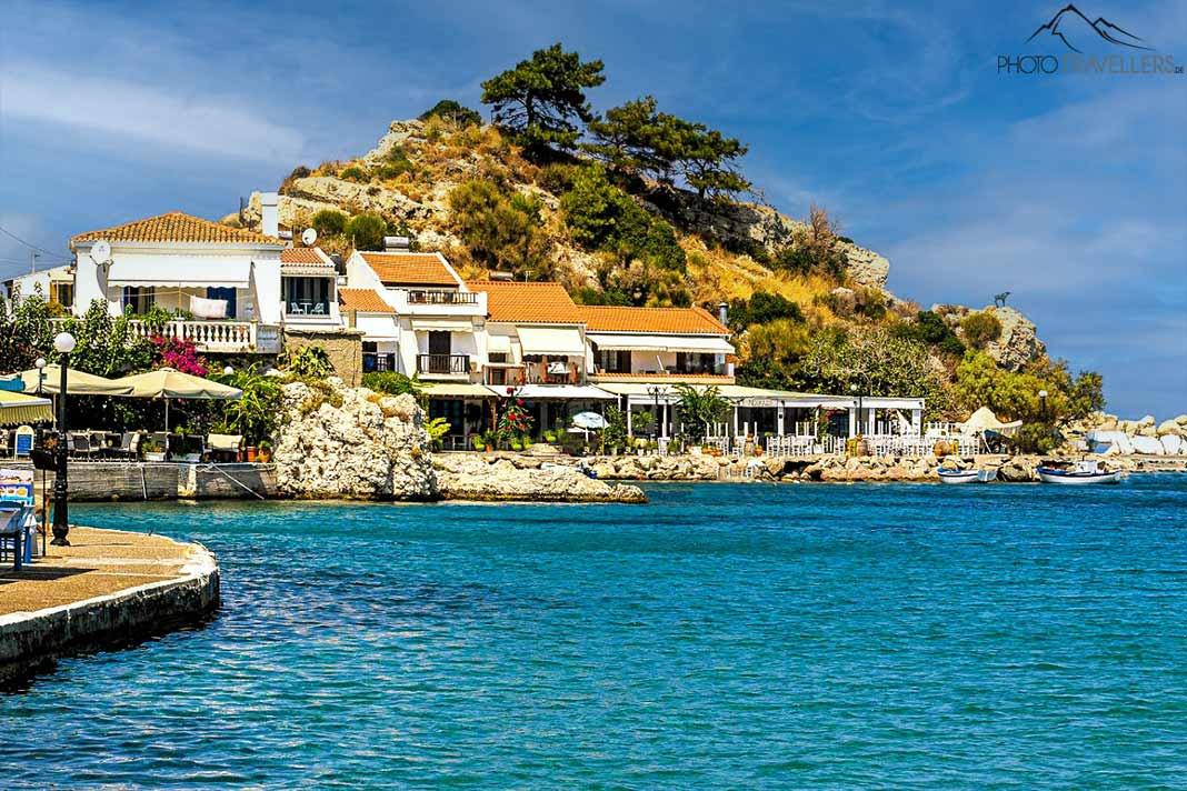 Casas brancas se aconchegam em uma rocha coberta de árvores no porto de Kokkari