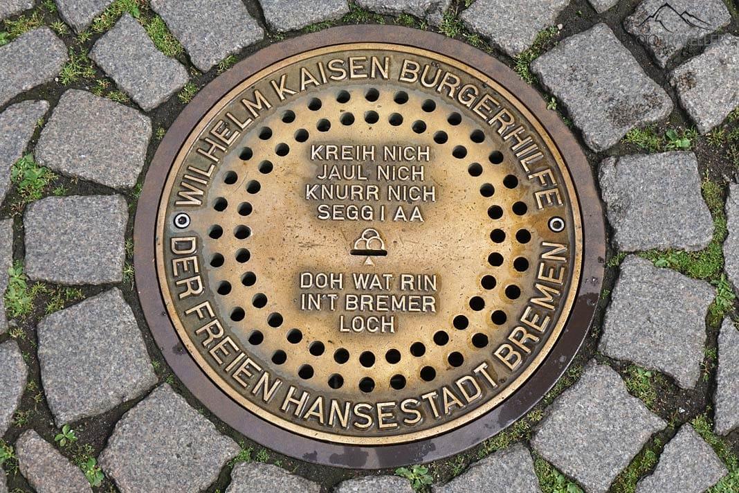 Le trou de Brême, un couvercle de canal doré avec l'inscription "Kreih nich, jaul nich, knurr nich, segg i aa, doh wat rin in't Bremer Loch"