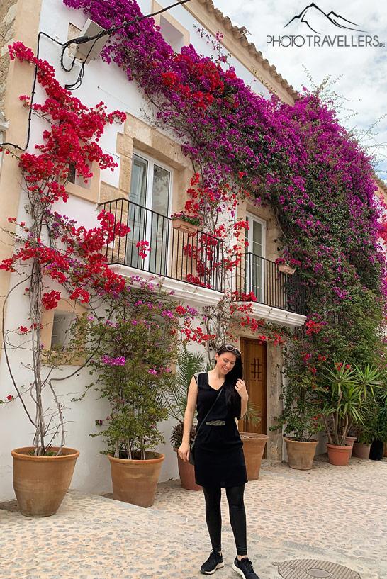 La blogueuse de voyage Biggi Bauer devant un mur avec des fleurs rouges et violettes dans la ville d'Ibiza