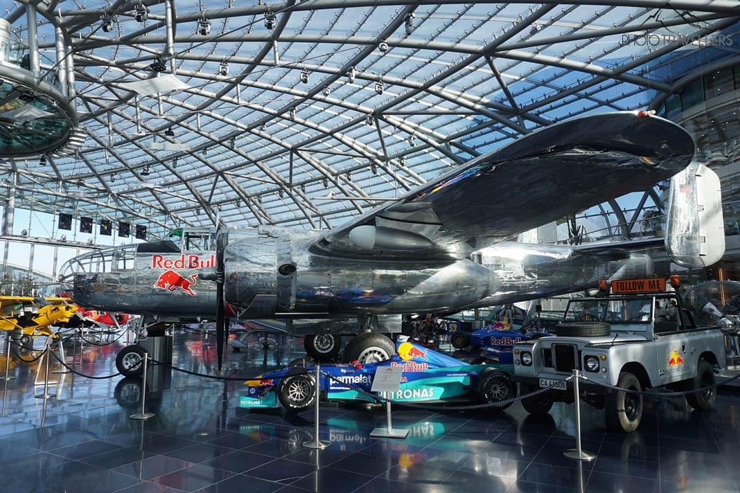 Un avión del tipo Douglas DC-6 con la inscripción 'Red Bull' detrás de un coche de Fórmula 1 y un Land Rover en el Hangar 7 en Salzburgo