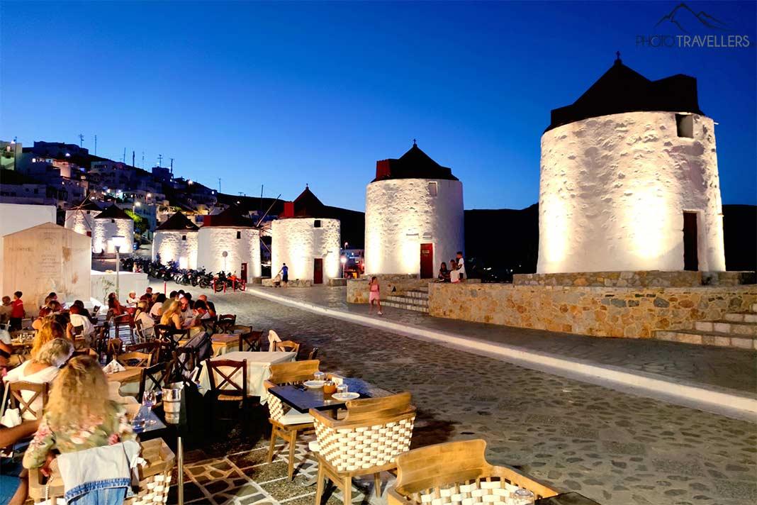 Les moulins à vent en pierre illuminés sous le ciel du soir avec des personnes à des tables au premier plan