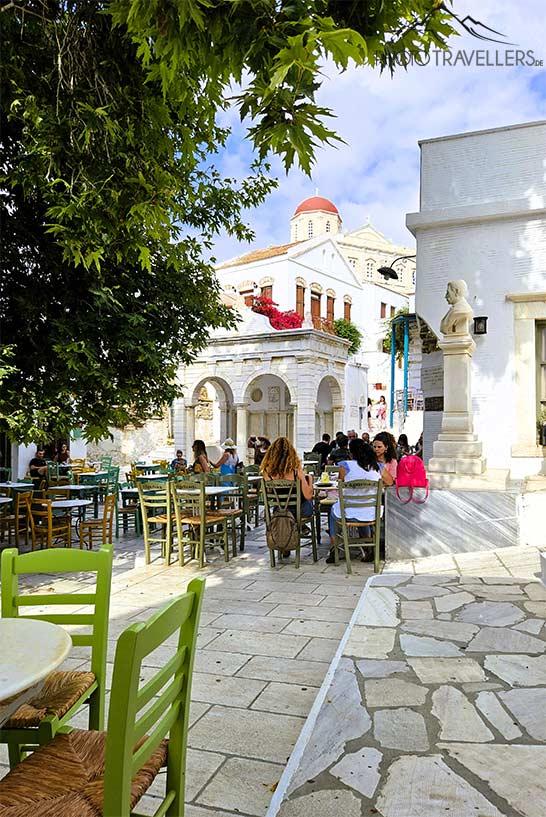 Des chaises colorées avec de nombreuses personnes ornent la place du village de Pyrgos autour d'un platane