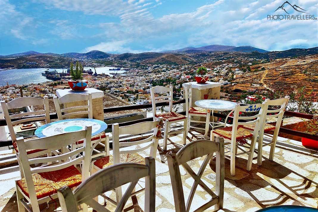Tables et chaises en bois vides sur une terrasse avec vue sur le port d'Ermoupoli