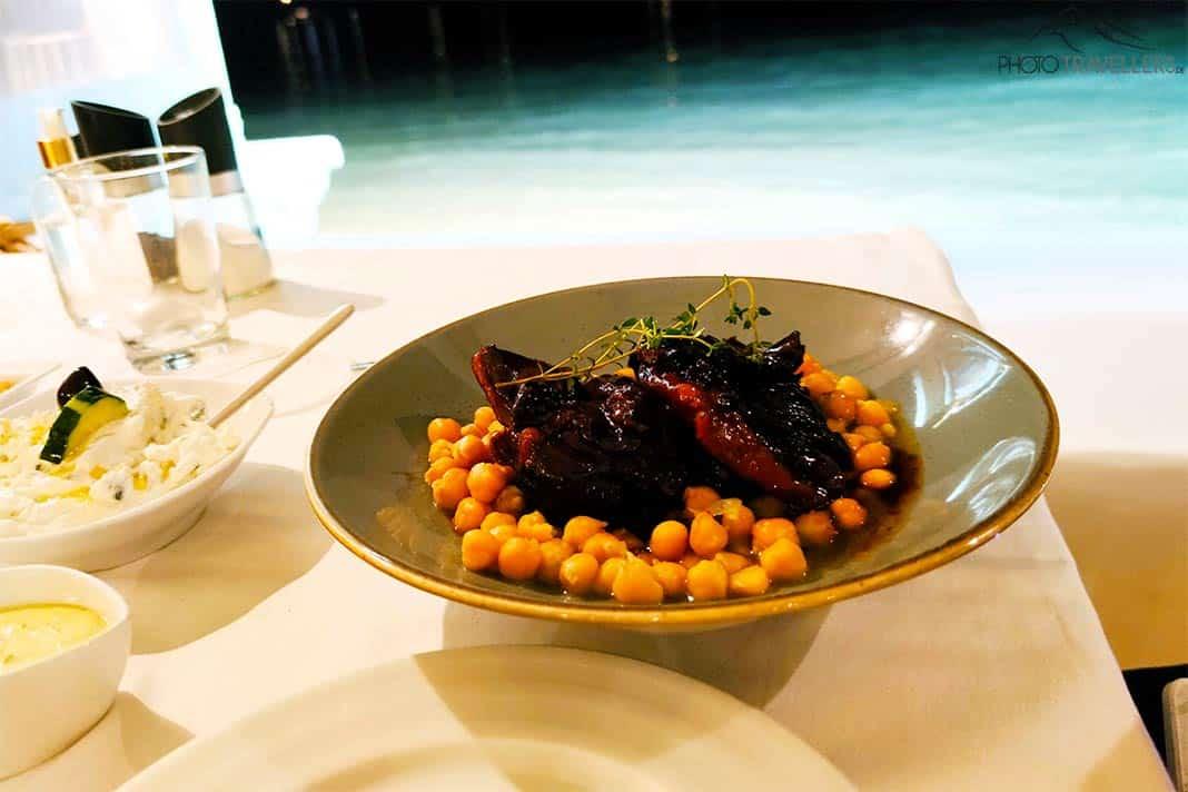 Un plat d'agneau mijoté avec des pois chiches sur une assiette avec la mer en arrière-plan