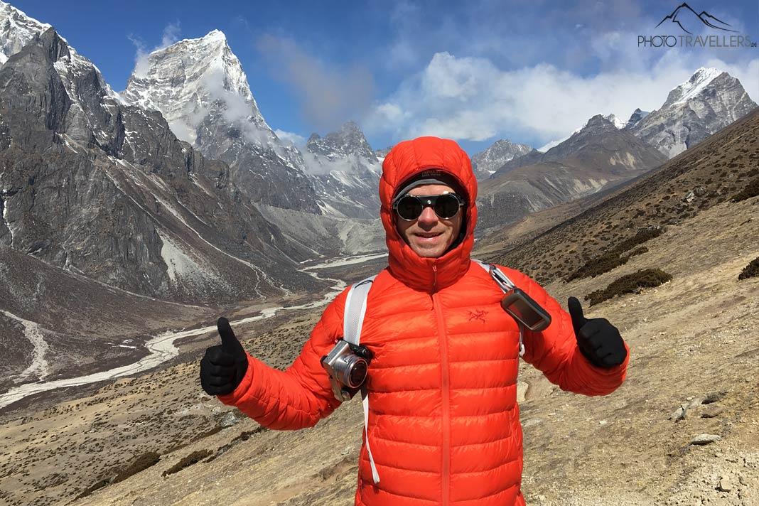 Le photographe Florian Westermann avec une doudoune orange et une caméra accrochée à son sac devant d'imposants sommets au Népal