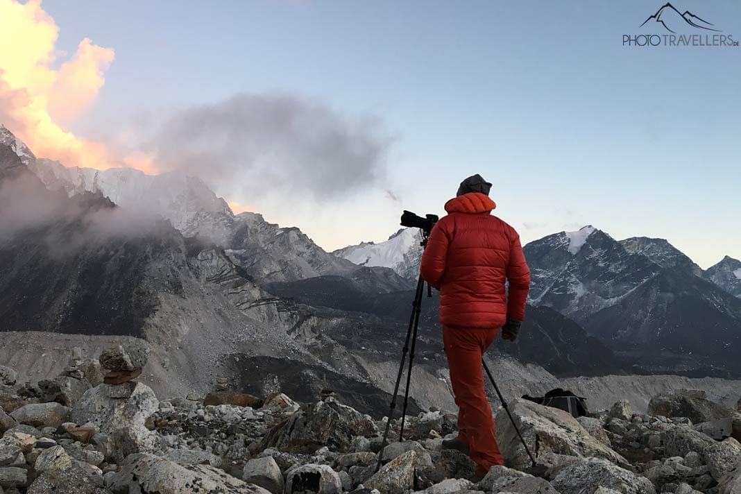 Le photographe Florian Westermann se tient le soir devant un imposant paysage de montagnes au Népal, devant lui un trépied avec une caméra