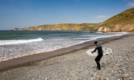 UK, Wales, Pembrokeshire, Newgale, surfer wearing wetsuit descending pebbly beach to seaJ9NPWB UK, Wales, Pembrokeshire, Newgale, surfer wearing wetsuit descending pebbly beach to sea