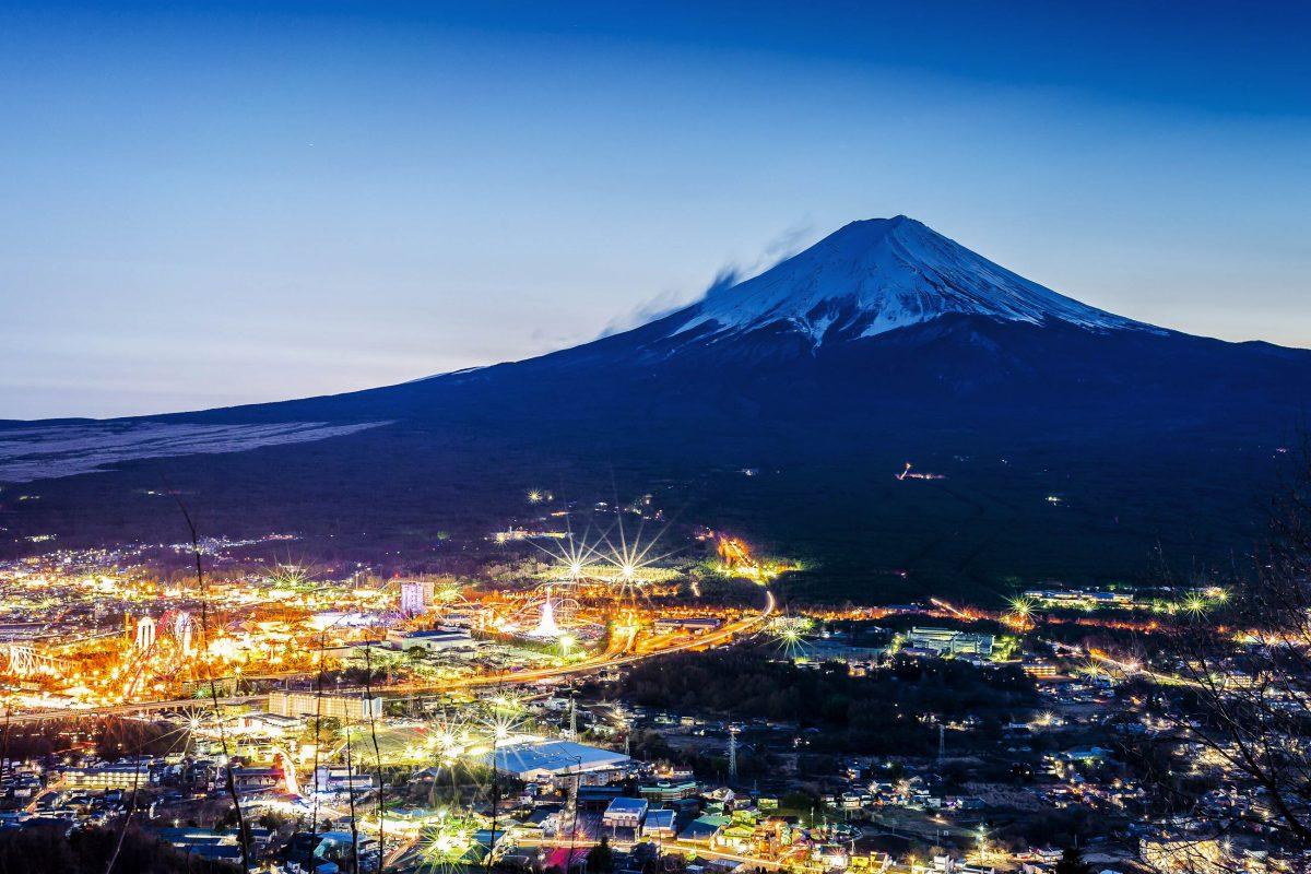 The brightly lit town of Fujiyoshida at dusk at the foot of Japan's famous Mount Fuji - © skyearth / Shutterstock